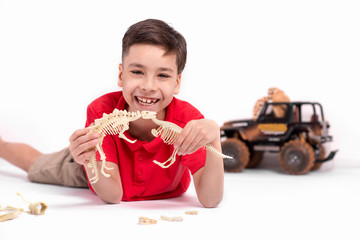 the boy the school student the brunette in a red t-shirt lies on a floor and plays with toy...