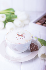 Coffee cappuccino with ceylon cinnamon, chocolates heart and white tulips on a white background. Free space