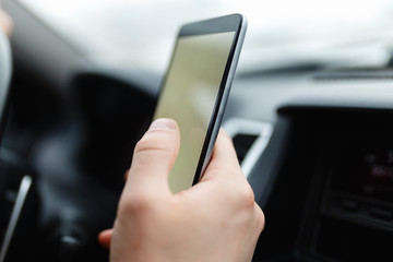 Modern smartphone with blank screen with copy space for your text or design, close-up of male driver hands using mobile phone in luxury car. Phone's touch screen and GPS navigation.