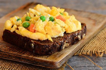 Scrambled eggs omelette idea. Home scrambled eggs omelette with vegetables on rye bread toasts. Healthy eating to lose weight. Rustic style. Closeup