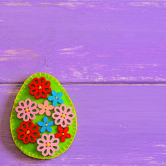 Beautiful Easter egg with wooden flower buttons. Felt Easter egg isolated on a purple wooden background with copy space for text. Felt egg craft. Happy Easter background