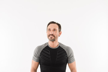 Fototapeta premium Portrait of masculine man 30s wearing sportswear looking upward on copyspace with smile and satisfied look after doing sports, isolated over white background