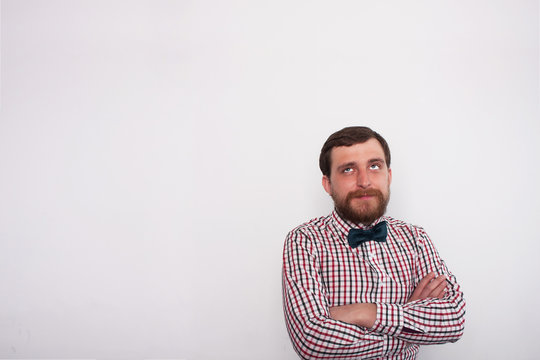 Young caucasian bearded hipster in casual clothes ponders. Thinkful man in studio with white background and copyspace. Businessman with crossed arms