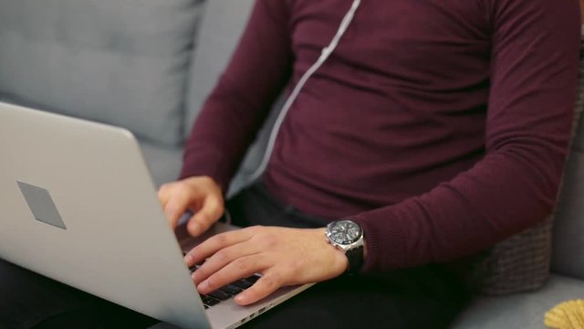 Close up view of a hot bearded man in headphones using the laptop, smiles towards the screen. Surfing the internet, having rest, being online. Male portrait, camera stabilizer shot