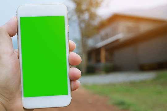 Hand Holding Shows Mobile Smartphone With Green Screen  And Touch Screen Of Smart Phone On House Backgrounds