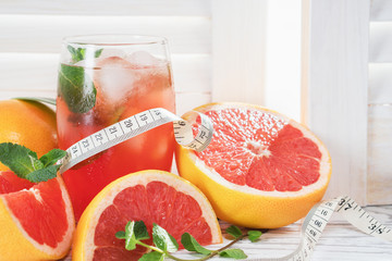 Fresh grapefruits and grapefruit juice, dumbbell and measuring tape, on rustic white wooden table opposite the blinds, fitness accessories. Concept of slimming, dieting and healthy nutrition.