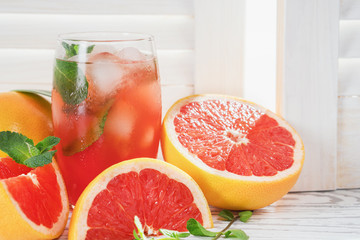 Fresh grapefruits and glass of grapefruit juice with ice and mint on rustic white wooden table opposite the blinds with copy space.  Close-up.