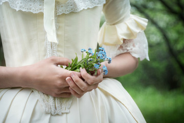a small bouquet of forget-me-not in the hands of a girl in a white dress