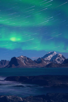 Northern lights, Aurora borealis with star trails over the rocky mountains, scenic night landscape, Lofoten Islands, Norway. Vertical image