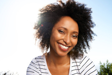 Close up attractive young african woman smiling outdoors against bright sunshine