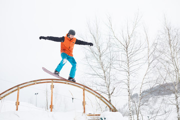 Naklejka na ściany i meble Image of young sportive man skiing on snowboard with springboard against background of trees