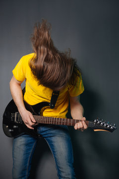 Man with long hair in yellow t-shirt, playing on electric guitar rock. Fashion studio portrait on a gray background.