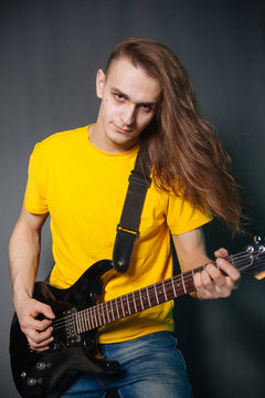 Man with long hair in yellow t-shirt, playing on electric guitar rock. Fashion studio portrait on a gray background.