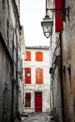 Narrow the street in Arles (Provence, France). Weathered stucco walls, red wooden shutters and...