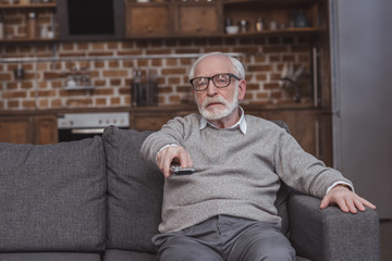 Fototapeta premium handsome grey hair man changing tv channels with remote control at home