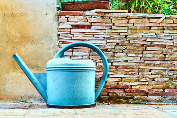 A watering can in front of a garden wall
