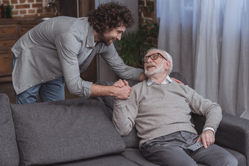 Fototapeta premium happy adult son and senior father holding hands at home