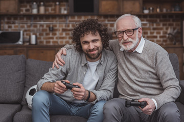 senior father hugging adult son while playing video game at home