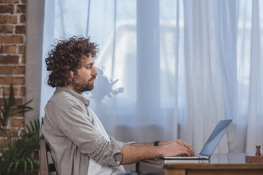 Side View Of Handsome Man Using Laptop At Table At Home