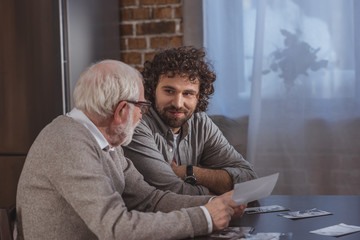 happy adult son and senior father looking at old photos at home