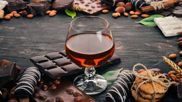A glass of cognac, brandy, whiskey and a set of chocolate with cookies and sweets. On a black wooden background. Copy space for text.