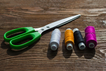 reels of multicolored threads and tailor scissors on wooden background