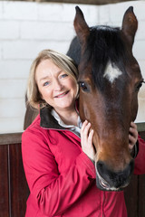 Portrait Of Mature Female Owner In Stable With Horse