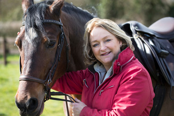 Portrait Of Mature Female Owner In Field With Horse