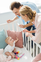 Obraz premium Smiling couple watching infant daughter in crib