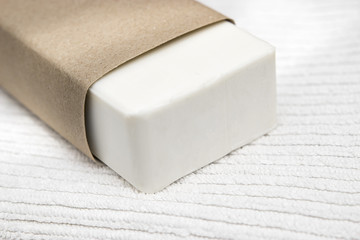 piece of white soap wrapped in a brown craft paper on a white towel background concept of body care