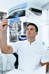 Handsome and attractive male dentist looking at dental x-ray.