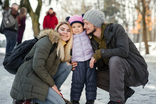 Two young happy parents pose with their charming little daughter in winter park