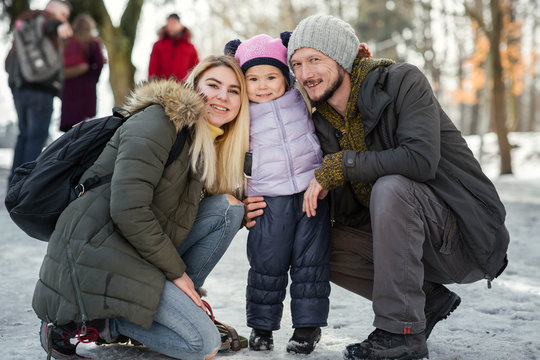 Two young happy parents pose with their charming little daughter in winter park