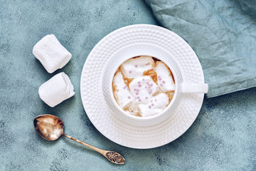 Coffee with marshmallow in white Cup on blue background close up, top view.