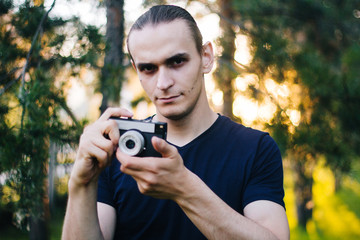 Handsome guy with a retro camera. A film camera in the hands of a young photographer. Model on the background of the park