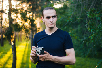 Handsome guy with a retro camera. A film camera in the hands of a young photographer. Model on the background of the park