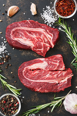 Raw beef steaks on a dark rustic background with spices and rosemary. Top view, close-up.