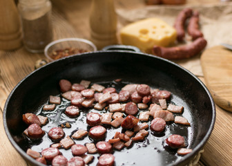 Bavarian sausages are sliced and fried in a frying pan.