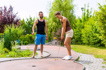 Couple, man and woman, playing miniature golf together outdoors