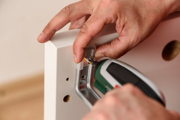 Close up on hands with cordless screwdriver assembling furniture