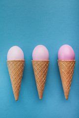 Pink easter eggs in waffle cones on blue background