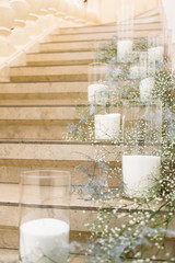 Vases with white candles and green branches stand on the footsteps in the hall