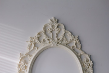 An empty, white vintage frame for the picture hanging on a white wall. Texture. Frame from the mirror with patterns