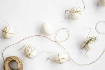 Easter eggs are minimalistically decorated with twine and gypsophila flowers. On a white background with a brown rope. Top view, flat lay