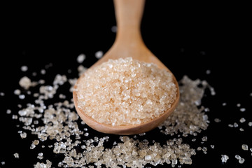 Brown sugar in wood spoon on black background.Components of The food is sweet delicious.