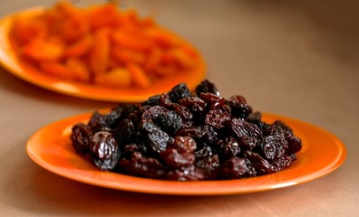 dry black grapes - raisin, red dried apricots on a red glass plate on a table
