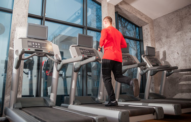 Man running on machine treadmill at fitness gym, back view