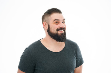 Studio shot of joyfully smiling bearded european male model in blue t-shirt, looking at camera with broad smile. Positive emotions, feelings and reaction