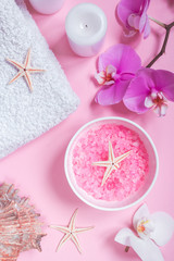 Spa background, flat lay layout with pink sea salt, candles and aroma oils and cosmetic care products on a pink background