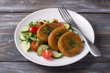 Carrot cutlets with amaranth, salad of fresh cucumbers and tomatoes on a wooden table. Delicious healthy homemade food